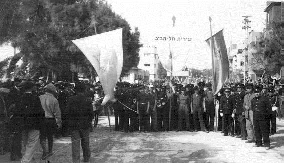 פורים בתל אביב: דגלי הלאום והעיר נישאים בראש התהלוכה, 1934. מתוך ארכיון ארווין יעקובי (PHAL1616064)