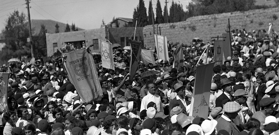 תלמידים מניפים מגוון דגלים ציוניים בחגיגות ה-70 למנחם אוסישקין בירושלים, 1933. (NZO\629749)