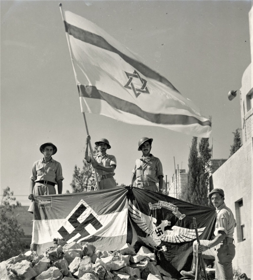 לוחמי מלחמת העצמאות מניפים את דגל ישראל לצד דגל נאצי, שמצאו במושבה הגרמנית בירושלים, 1948. (PHG\1309291)