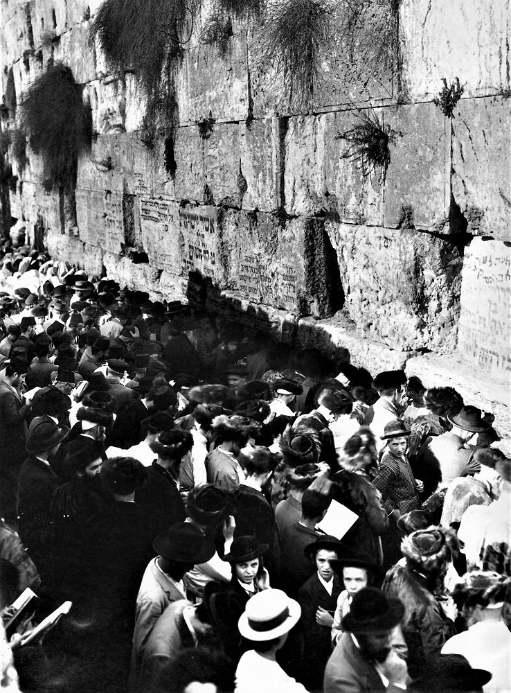 יהודים מתפללים ליד הכותל המערבי, ועל אבני הכותל כתובים שמות ופסוקים בעברית. (PHAL\1655567)