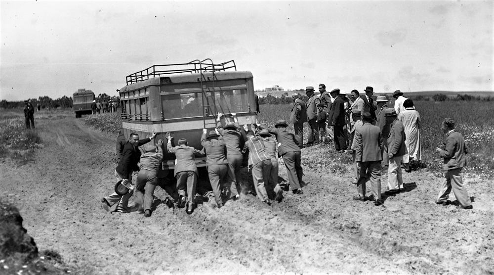 תיירים מדרום אפריקה דוחפים את האוטובוס התקוע בדרך לביקור במושב עין ורד, 1935. (NZO\632461)