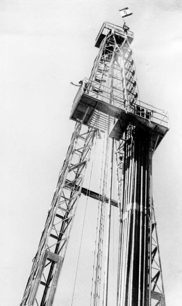 הנפת דגל ישראל בראש מגדל הקידוח לאחר מציאת הנפט בחלץ, ספטמבר 1955. (PHKH\1294713)
